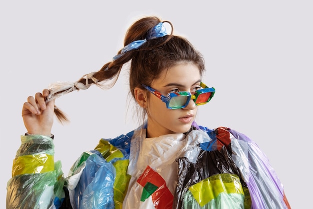 Woman wearing plastic on white wall. Female model in clothes and shoes made of garbage. Fashion, style, recycling, eco and environmental concept. Too much pollution, we're eating and taking it.