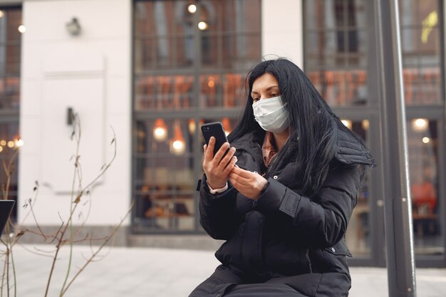 携帯電話を使用して通りに座っている防護マスクを着ている女性