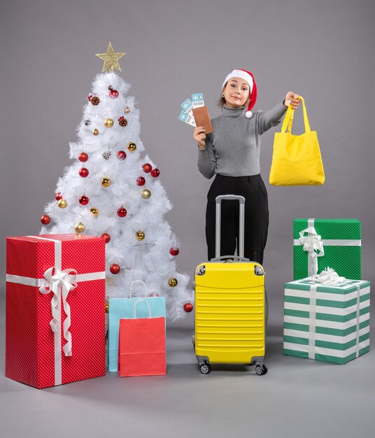 Woman wearing Santa Claus hat with luggage next to Christmas tree