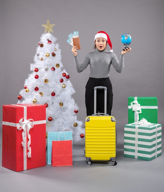 Free photo woman wearing santa claus hat with luggage next to christmas tree