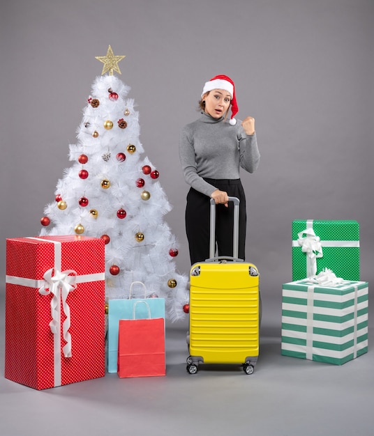 Woman wearing santa claus hat with luggage next to christmas tree