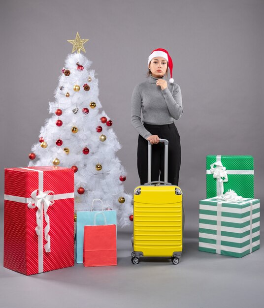 Donna che indossa il cappello di babbo natale con i bagagli accanto all'albero di natale