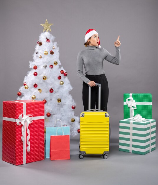 Женщина в шляпе Санта-Клауса с багажом рядом с елкой