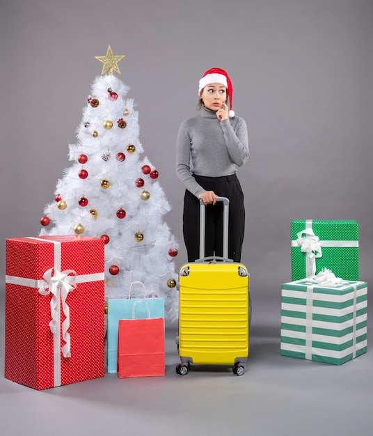 クリスマスツリーの横に荷物とサンタクロースの帽子をかぶっている女性
