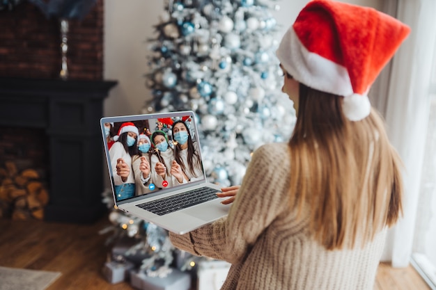 Woman wearing santa hat while speaking with online friend on laptop
