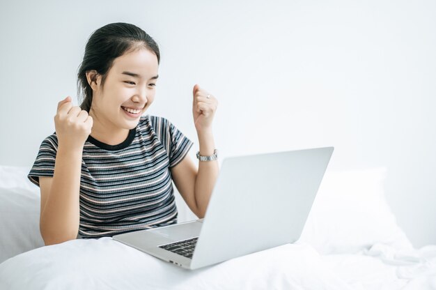 Женщина в полосатой рубашке на кровати и счастливо играть на ноутбуке.