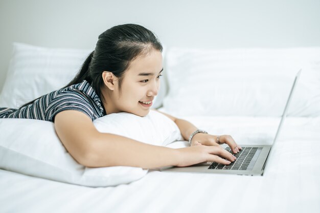 A woman wearing a striped shirt on the bed and playing a laptop.