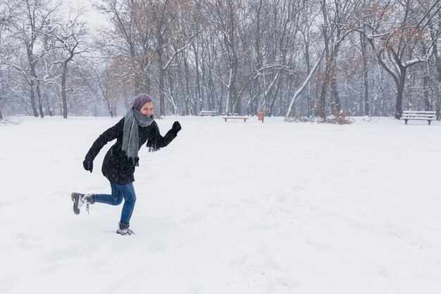 冬の雪に覆われた土地を走る暖かい服を着ている女性