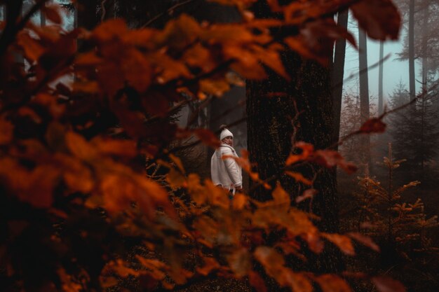 Woman wearing white jacket standing near tree in forest