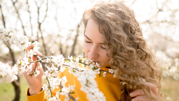 Foto gratuita donna che indossa i fiori sententi l'odore della camicia gialla