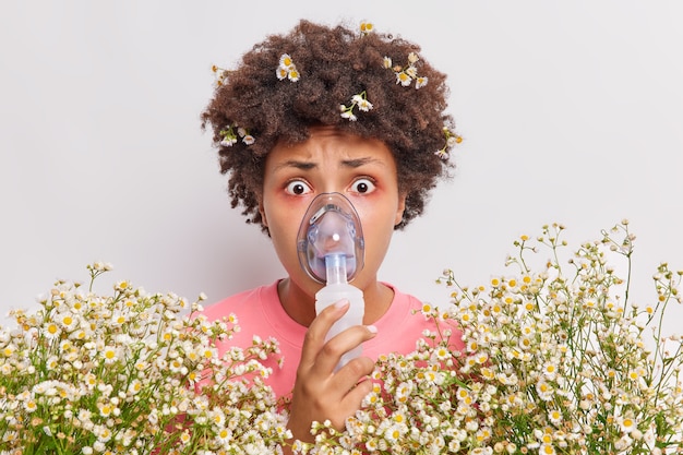 woman wears nebulizer mask for breathing free stares impressed has red eyes allergic reaction to camomile poses indoor on white 