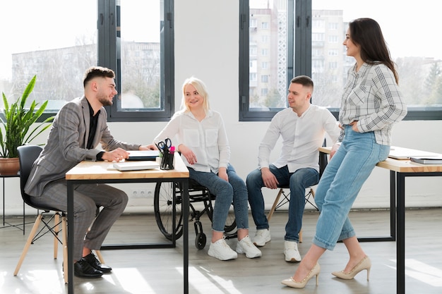 Woman in wheelchair and coworkers at office conversing