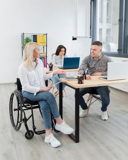 Woman in wheelchair discussing with coworker at desk