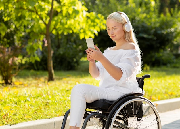 Woman in wheelchair listening to music outdoors with cellphone
