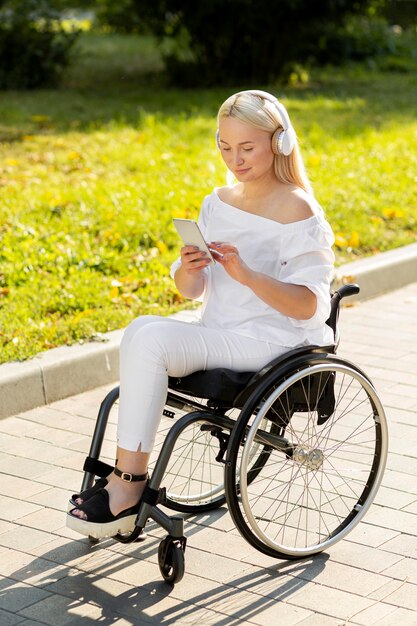 Woman in wheelchair listening to music outdoors with smartphone