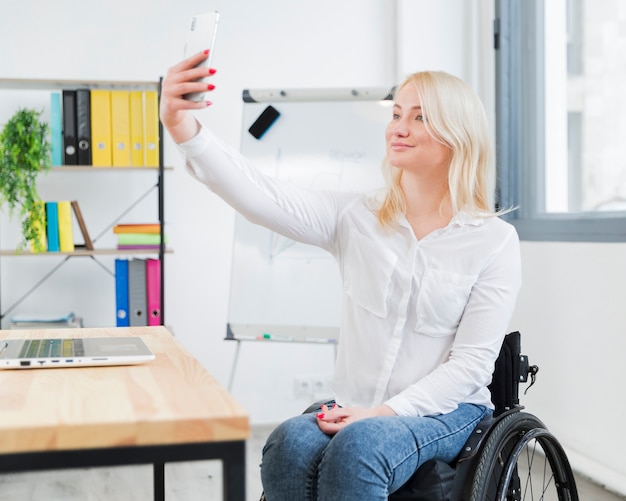 Woman in wheelchair taking selfie at work