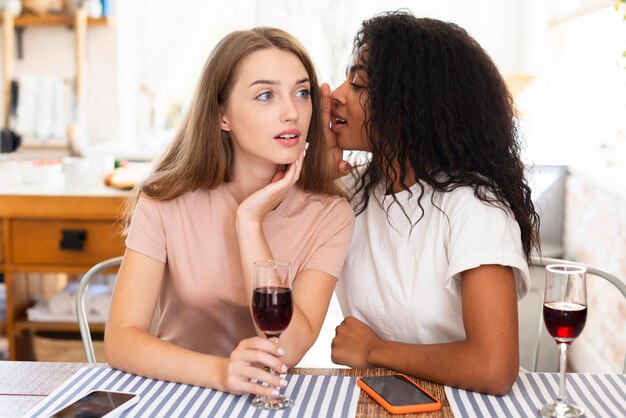 Woman whispering a secret to her friends while having wine