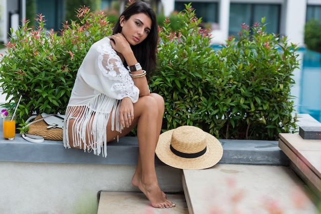 woman in white bikini posing in modern hotel in Thailand wearing stylish boho beachwear