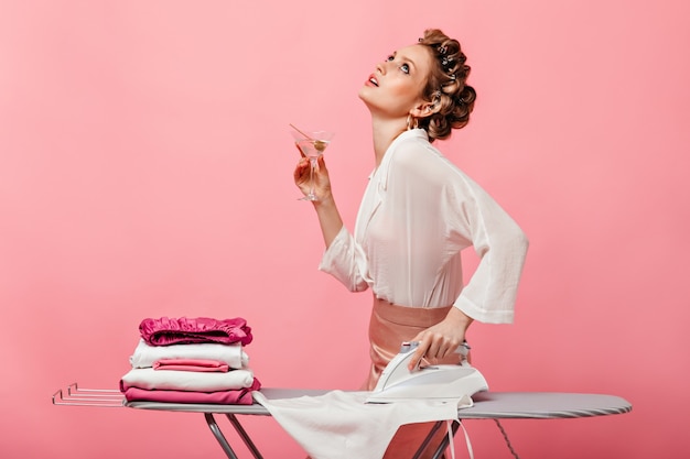 woman in white blouse drinks martini and ironing t-shirt on ironing board