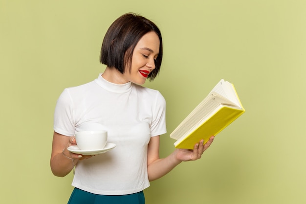 woman in white blouse and green skirt holding cup of tea and reading a book 