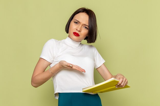 woman in white blouse and green skirt holding and reading yellow book