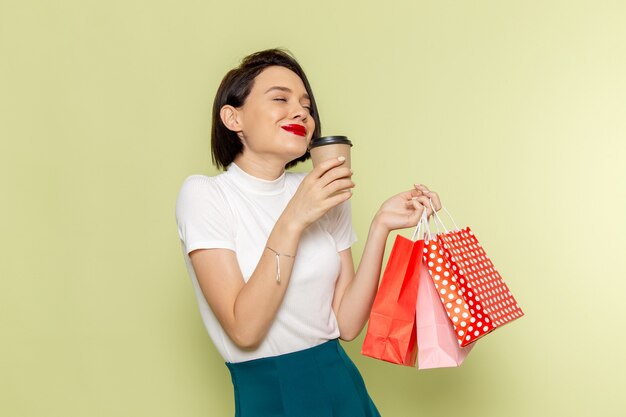 woman in white blouse and green skirt holding shopping packages and coffee 