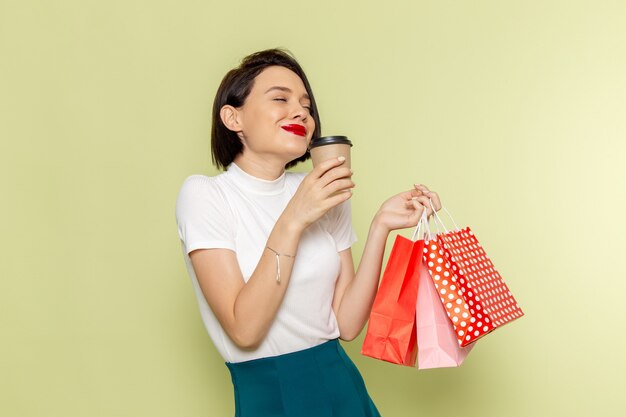 ショッピングパッケージとコーヒーを保持している白いブラウスと緑のスカートの女性