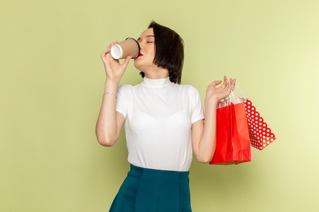 ショッピングパッケージを押しながらコーヒーを飲みながら白いブラウスと緑のスカートの女性