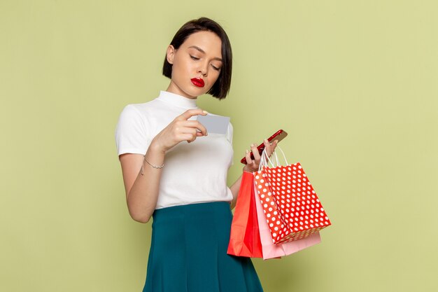 ショッピングパッケージと電話女性服ファッションモデルを保持している白いブラウスと緑のスカートの女性