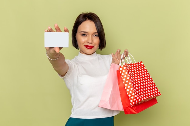 Free photo woman in white blouse and green skirt holding shopping packages and showing white card