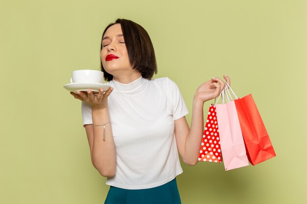 woman in white blouse and green skirt holding shopping packages with cup of tea 