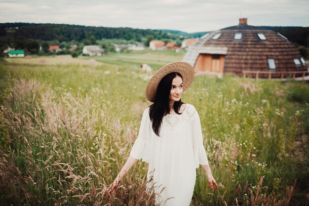 Woman in white dress and hay hat walks across the field 