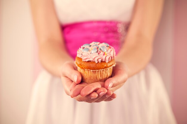 Женщина в белом платье держит розовый кекс