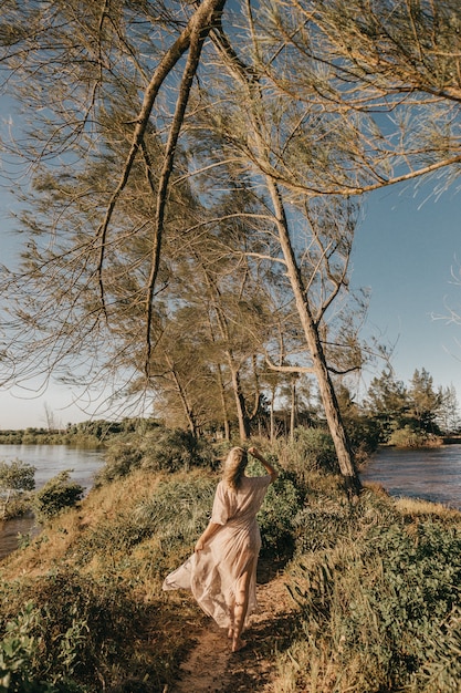 женщина в белом платье гуляет босиком по маленькому травянистому участку в окружении воды