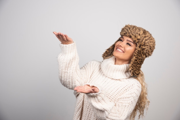 Woman in white knitted sweater holding open space. 