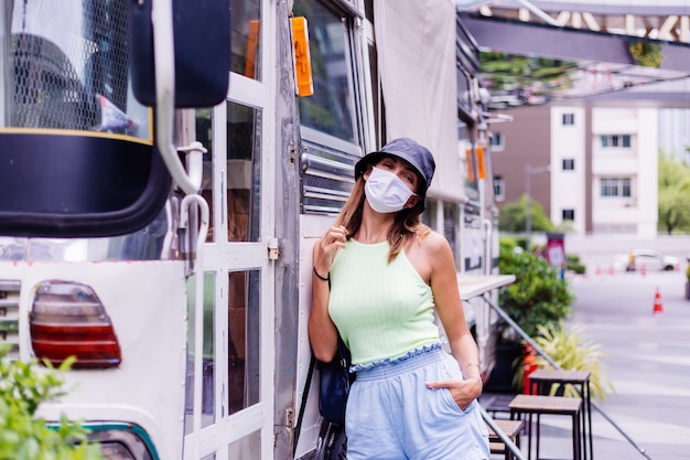 Woman in white medical mask walk around city stands by bus cafe on city square