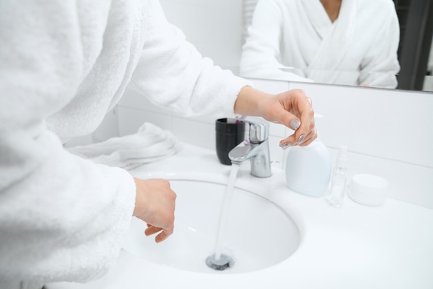Foto gratuita donna in veste bianca in piedi vicino al lavandino e lavarsi le mani