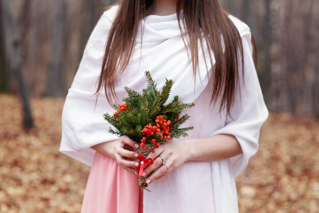 Woman in white shawl holds bouquet of red berries and fir