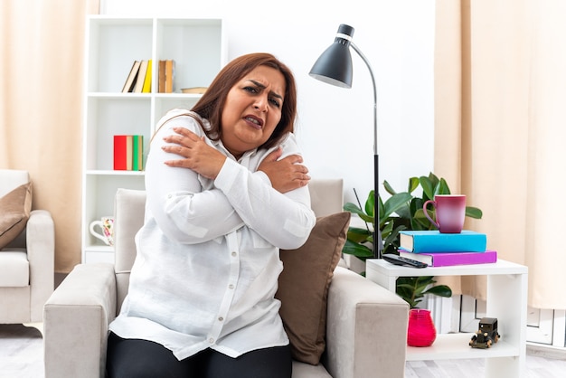 Woman in white shirt and black pants  worried and scared sitting on the chair in light living room