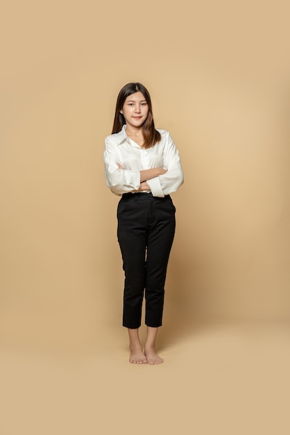 A woman in a white shirt and black trousers stands with her arms folded