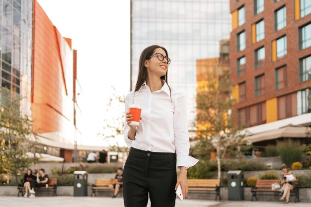 行くためにコーヒーを持っている白いシャツの女性