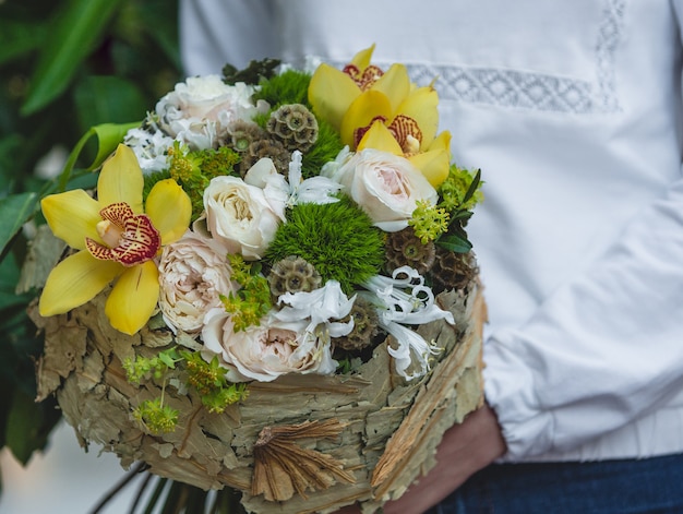 Woman in white shirt holding a pale colors of flowers in paper bouquet