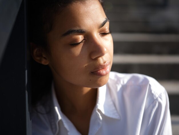 woman in white shirt posing with eyes closed outdoors on a warm sunny day. Selective focus