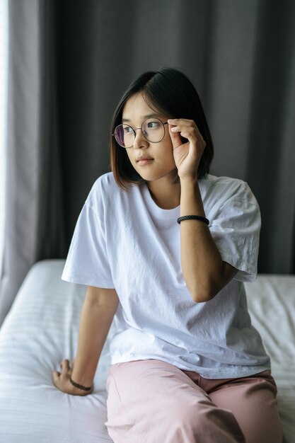 A woman in a white shirt sitting on the bed and looking out.