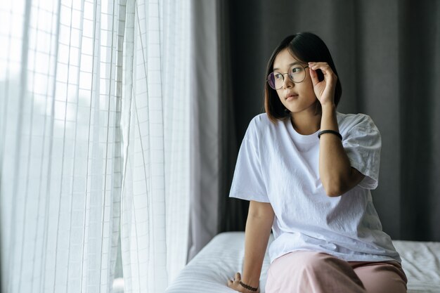 Женщина в белой рубашке сидит на кровати и смотрит.
