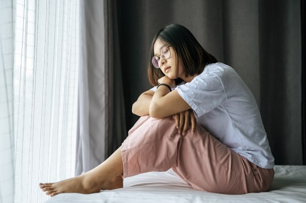 A woman in a white shirt sitting on the bed and looking out.