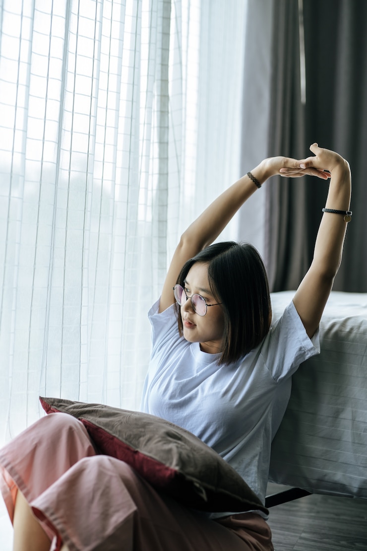 무료 Photo 침대에 앉아서 두 팔을 올리는 흰 셔츠에 여자.