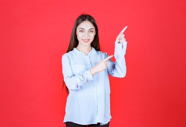 woman in white shirt standing on red wall and showing right side. 