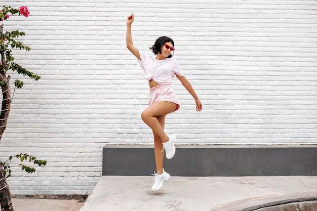 woman in white sneakers jumping on street. Full length view of dancing woman enjoying summer.