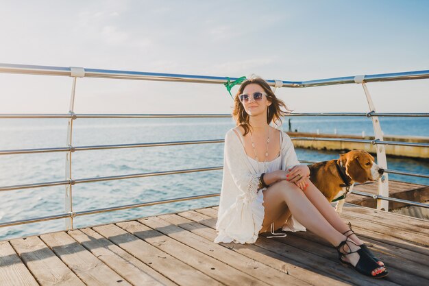 woman in white summer dress playing with dog by the sea